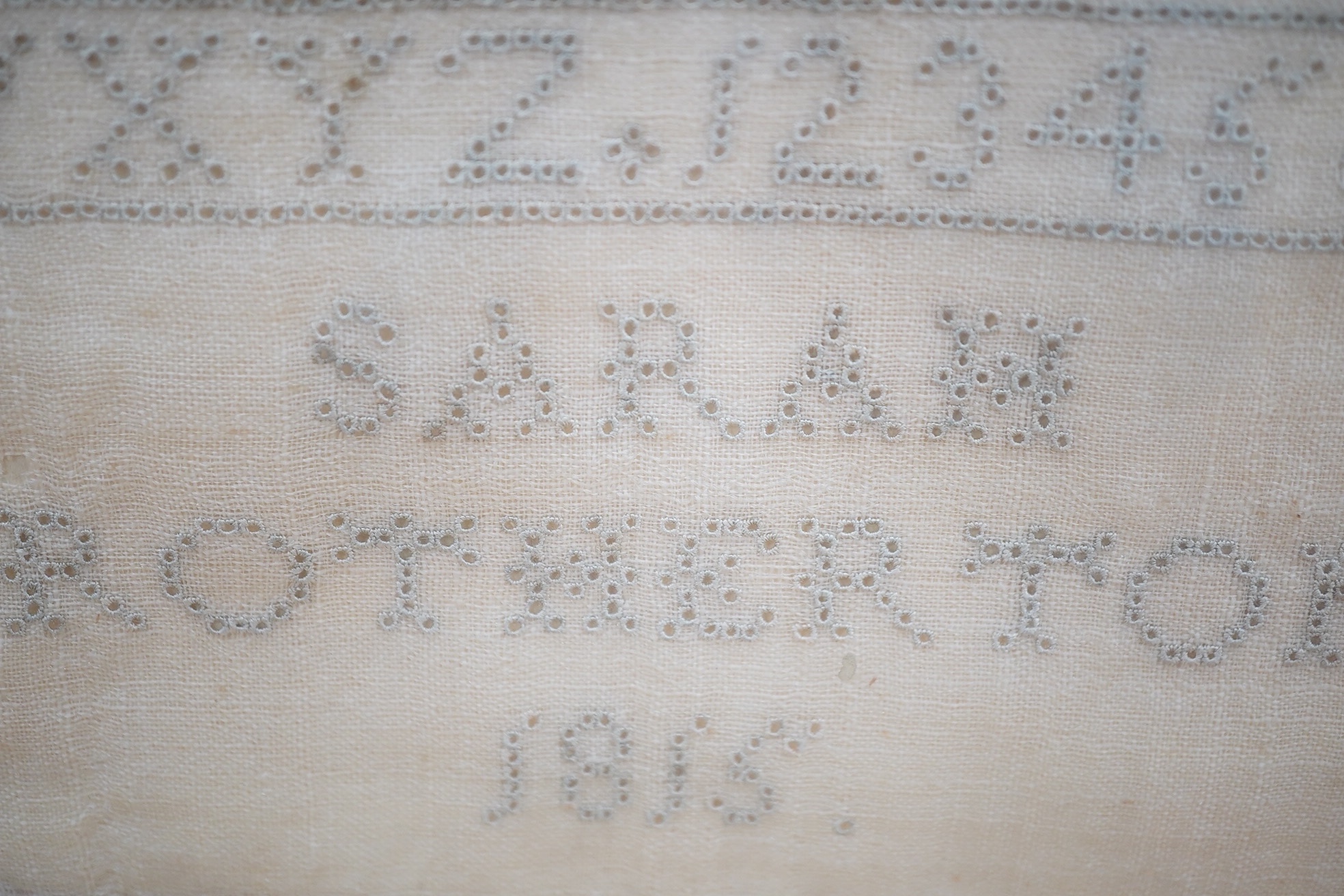 A George III needlework sampler, by Sarah Brotherton, dated 1815, a simple graduated monochrome alphabet sampler, the top worked in fine embroidery stitches, the main part in fine button holestitch around the shapes of c